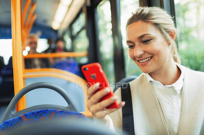 Усміхнена молода жінка використовує смартфон в автобусі — стокове фото