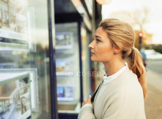 Jeune femme regardant les listes de maisons en vitrine — Photo de stock