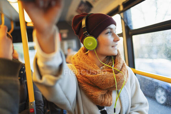 Young woman in stocking cap and scarf listening to music with headphones on bus — Stock Photo