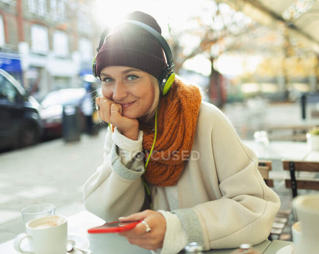 Портрет впевнена молода жінка слухає музику з навушниками та mp3 плеєром на осінньому тротуарному кафе — стокове фото