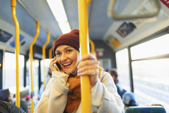 Une jeune femme souriante en train de parler au téléphone intelligent dans un autobus — Photo de stock