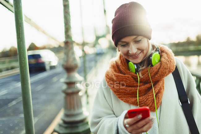Молода жінка в панчішній шапці і шарф смс з смартфоном — стокове фото