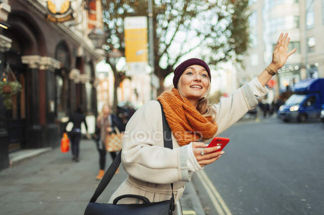 Женщина со смартфоном приветствует такси на городской улице — стоковое фото