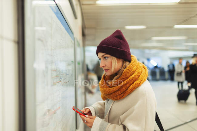 Mujer joven con teléfono inteligente que comprueba el mapa del metro - foto de stock
