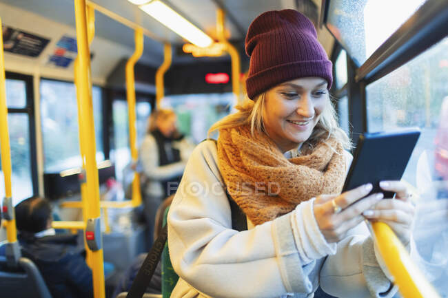 Молодая женщина в шапке-ушанке и шарфе с цифровым планшетом в автобусе — стоковое фото