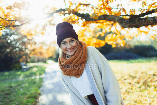 Retrato feliz mujer joven en gorra de siembra y bufanda en soleado parque de otoño. - foto de stock
