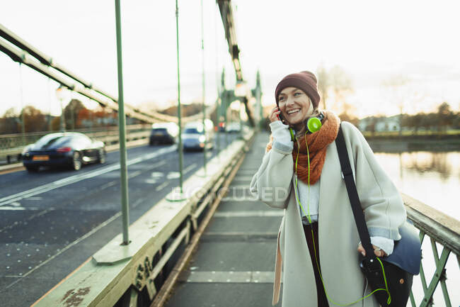 Jovem mulher no meia tampa e cachecol falando no telefone inteligente na ponte — Fotografia de Stock