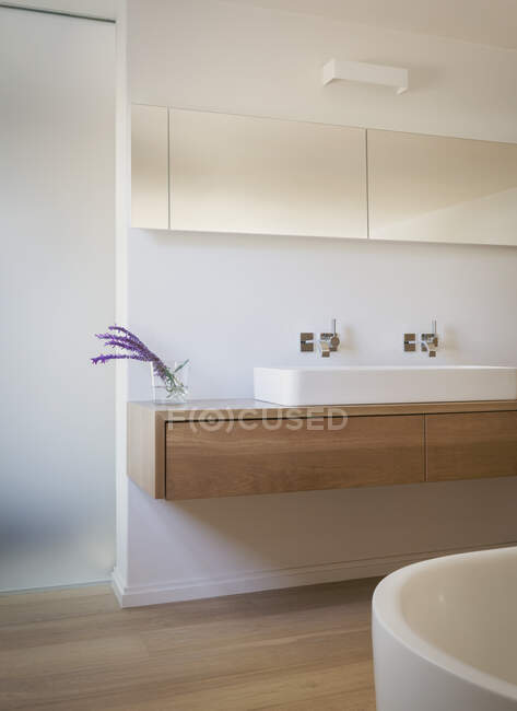 Baño blanco moderno con flores púrpuras en el jarrón. - foto de stock