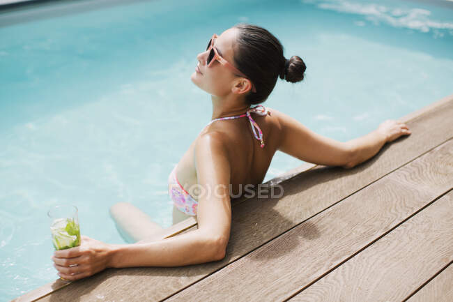 Ніжна жінка з коктейлем відпочиває в сонячному літньому басейні — стокове фото