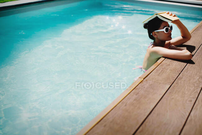 Donna che tiene libro in testa nella soleggiata piscina estiva — Foto stock