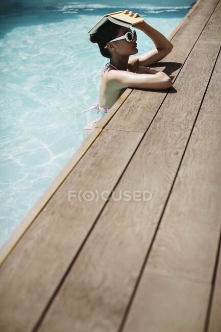 Woman holding book overhead in sunny summer swimming pool — Stock Photo