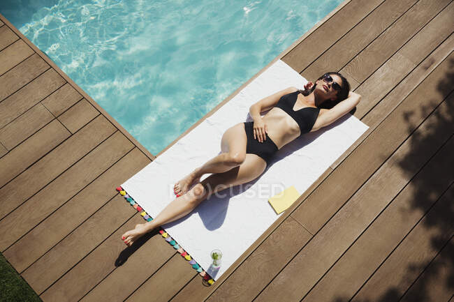 Ніжна жінка в чорному бікіні розслабляється, засмагає в сонячному літньому басейні — стокове фото
