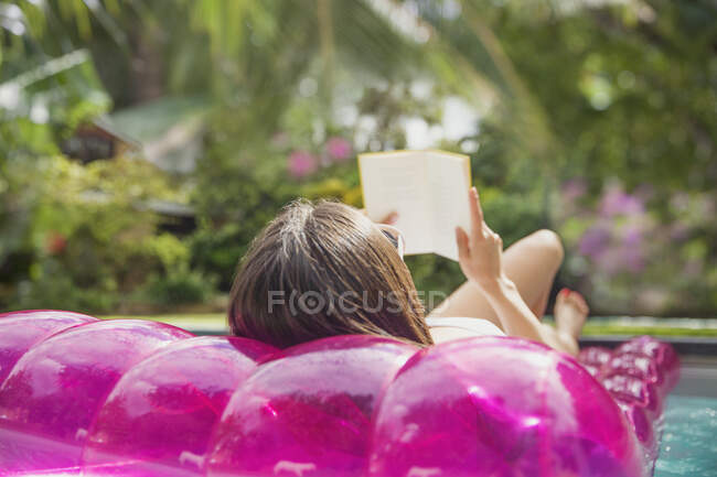 Жінка розслабляється, читає книгу на надувній плоті в басейні — стокове фото