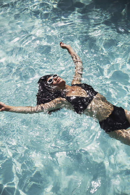 Heitere Frau im schwarzen Bikini schwimmt im sonnigen Sommerpool — Stockfoto