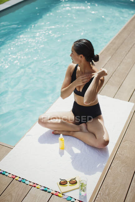 Donna che applica la protezione solare a bordo piscina estiva soleggiata — Foto stock