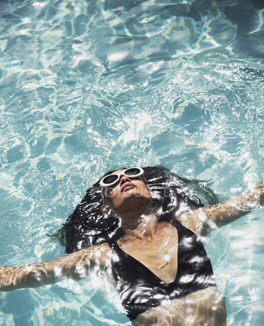 Sereno, mulher sensual em óculos de sol e biquíni flutuando na piscina ensolarada — Fotografia de Stock