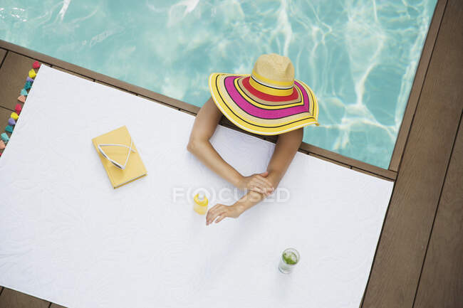 Женщина в шляпе для загара наносит солнцезащитный крем в бассейне — стоковое фото