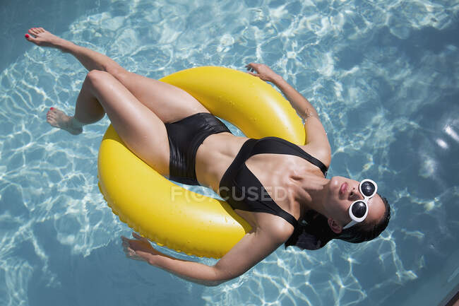 Mulher sensual em biquíni preto flutuando no anel inflável na piscina ensolarada de verão — Fotografia de Stock