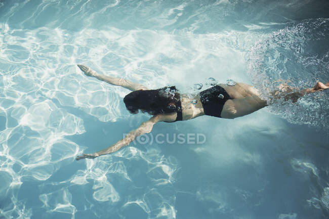 Женщина в бикини плавает под водой в солнечном бассейне — стоковое фото