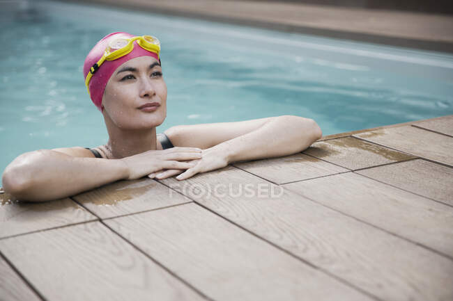Confident woman in swimming cap and goggles leaning on edge of swimming pool — Stock Photo