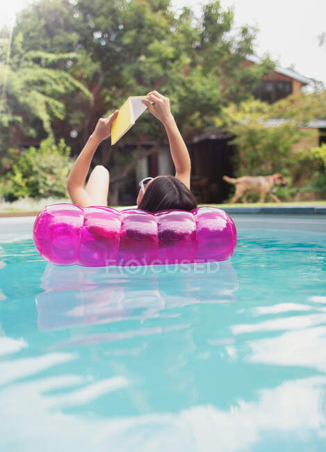Жінка розслабляється, читає книгу на надувній плоті в сонячному літньому басейні — стокове фото