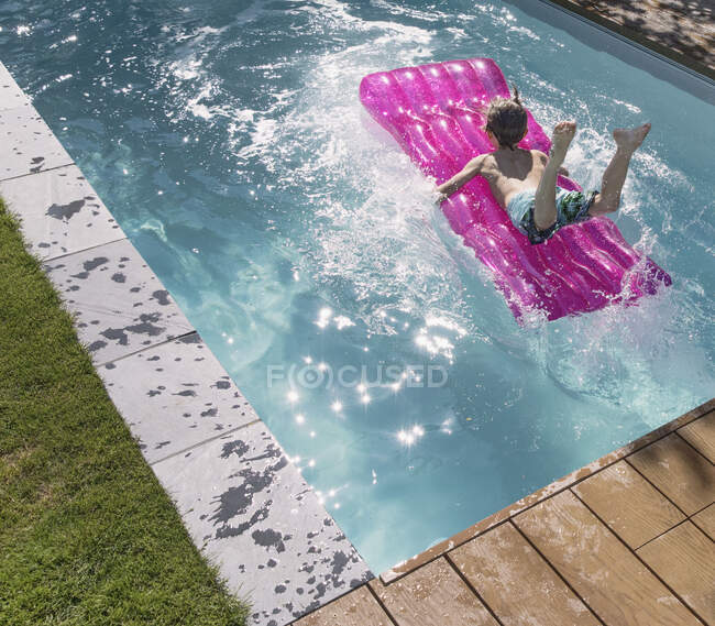 Играющий мальчик прыгает на надувном плоту в солнечном летнем бассейне — стоковое фото