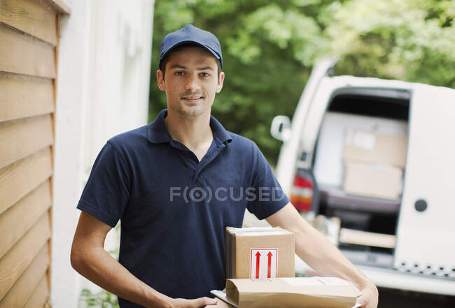 Retrato confiante entregador com pacotes na porta da frente — Fotografia de Stock