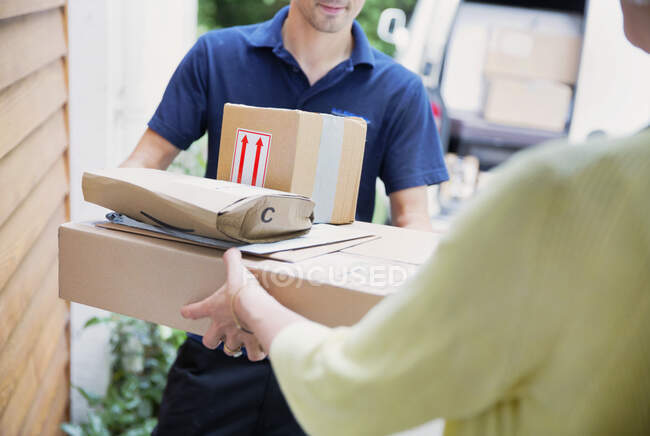 Entregador entregando paquetes a la mujer en la puerta principal - foto de stock