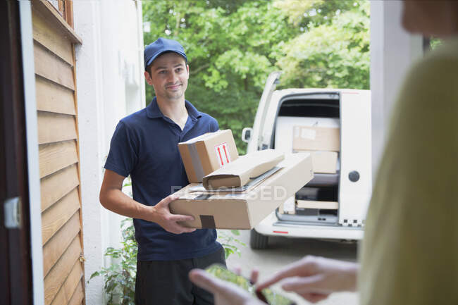 Smiling deliveryman watching woman signing smart phone at front door — Stock Photo