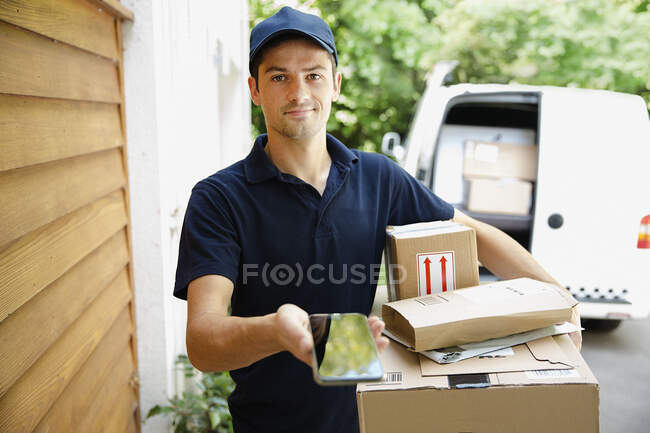 Portrait confident deliveryman with smart phone at front door — Stock Photo