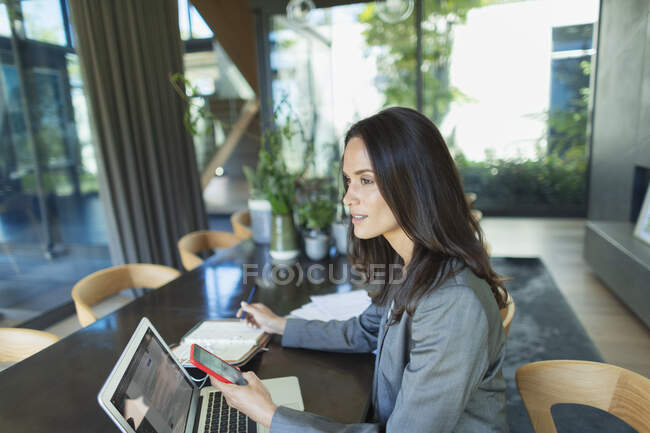 Деловая женщина работает из дома, используя смартфон и ноутбук — стоковое фото