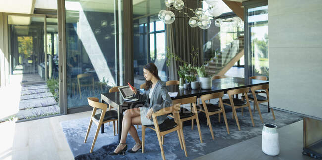 Empresária trabalhando em casa, usando telefone inteligente na mesa de jantar moderna — Fotografia de Stock
