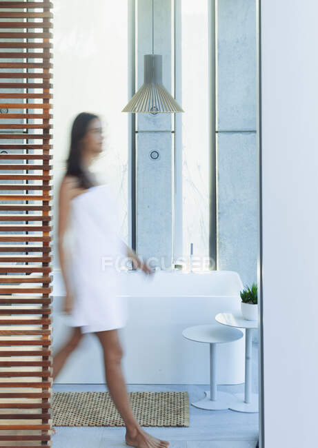 Mujer envuelta en una toalla caminando en lujoso y moderno baño - foto de stock