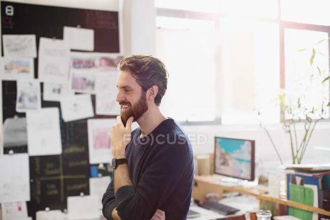 Happy creative businessman rubbing beard in office — Stock Photo