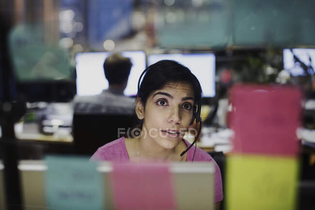 Geschäftsfrau mit Headset blickt auf Klebezettel, Planung im Büro — Stockfoto