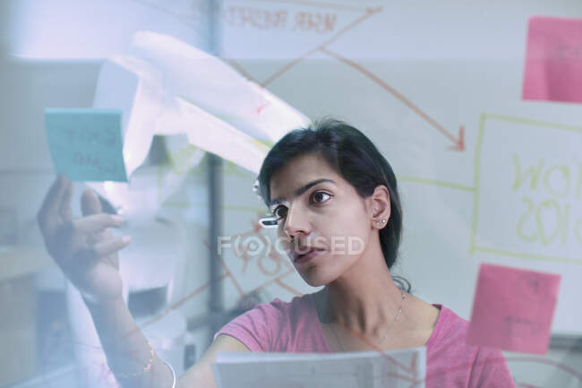 Mujer de negocios revisando notas adhesivas y diagrama de flujo, planificación en la oficina - foto de stock
