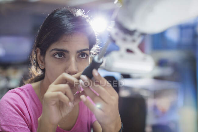 Орієнтована жінка-інженер з викруткою, що фіксує роботизовану руку — стокове фото