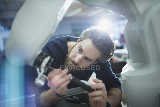 Концентрированный мужчина-инженер с отвёрткой, фиксирующей роботизированную руку — стоковое фото