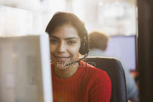 Портрет улыбается, уверенная деловая женщина с наушниками, работающая за компьютером в офисе — стоковое фото