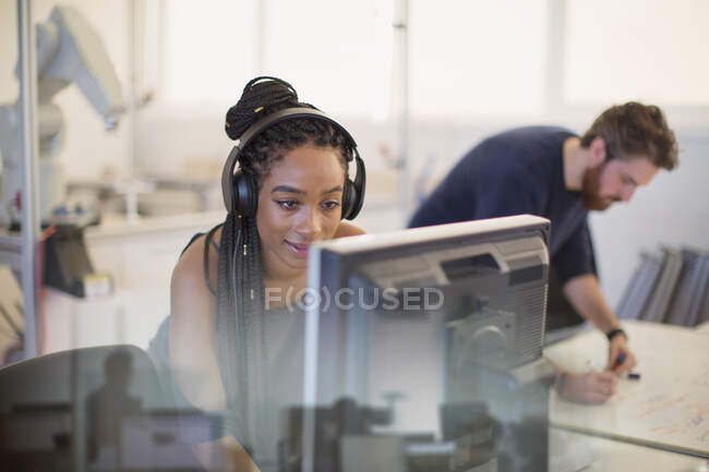 Ingénieur féminin avec écouteurs utilisant l'ordinateur dans le bureau — Photo de stock