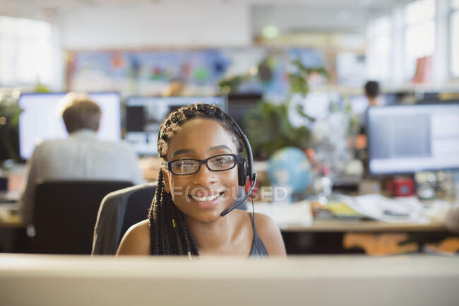 Portrait confident businesswoman with headset working at computer in open plan office — Stock Photo
