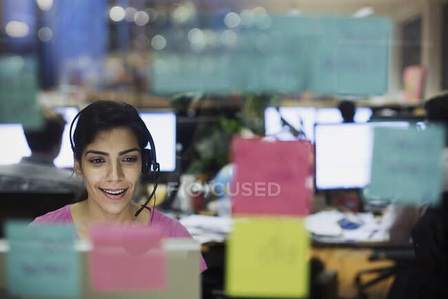 Geschäftsfrau mit Headset arbeitet am Computer im Büro hinter Klebezetteln — Stockfoto
