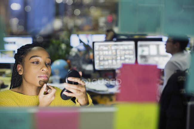 Donna d'affari che applica il trucco con specchio compatto in ufficio — Foto stock