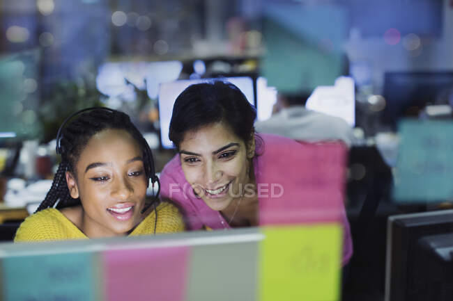 Mujeres de negocios sonrientes que trabajan en la computadora detrás de notas adhesivas - foto de stock
