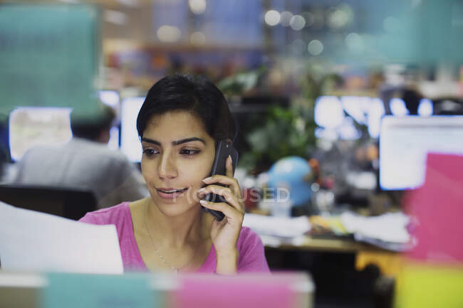 Geschäftsfrau telefoniert mit Smartphone und liest Papierkram im Büro — Stockfoto