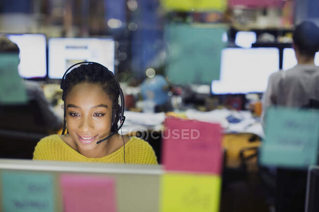 Бізнес-леді з гарнітурою, що працює за комп'ютером за клейовими нотами — стокове фото
