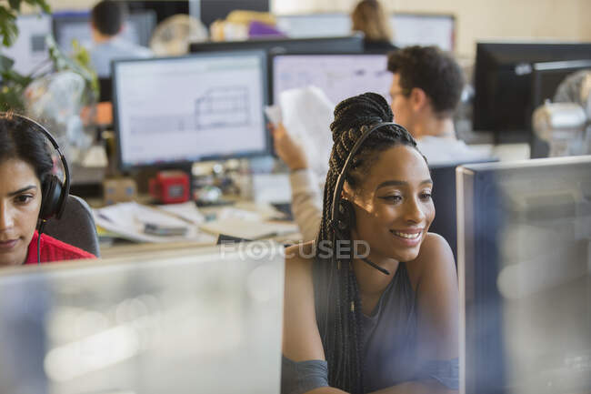 Empresária sorridente com fone de ouvido trabalhando no computador no escritório — Fotografia de Stock