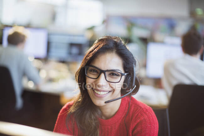 Retrato confiado, mujer de negocios sonriente con auriculares trabajando en la oficina - foto de stock