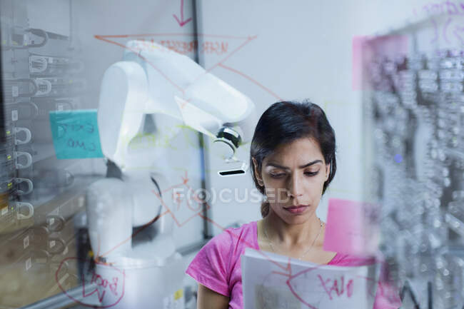 Female engineer with paperwork planning, programming robotic arm — Stock Photo