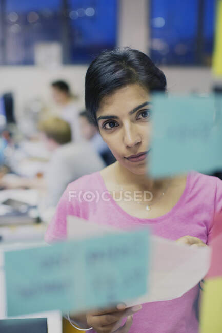 Focused businesswoman planning, looking at adhesive notes in office — Stock Photo